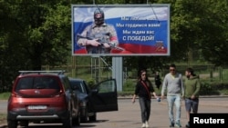 FILE - People walk near a banner in support of the Russian Army, in the town of Vyborg, Leningrad Region, Russia, May 28, 2023. The banner reads "We love you! We are proud of you! We are waiting for you with a victory!"
