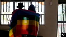 FILE - A gay Ugandan couple cover themselves with a pride flag as they pose for a photograph in Uganda, March 25, 2023.