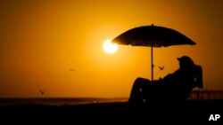 FILE - A person rests under an umbrella as the sun sets, Sept. 12, 2023, in Newport Beach, Calif. 