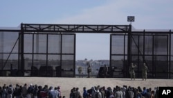FILE - Migrants who crossed the border from Mexico into the U.S. wait next to the U.S. border wall where U.S. Border Patrol agents stand guard, seen from Ciudad Juarez, Mexico, March 30, 2023.