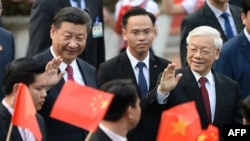 资料照片：2017年11月12日，在河内举行的欢迎仪式上，中国国家主席习近平(左)和越南共产党总书记阮富仲(右)向举着越南和中国国旗的学生挥手致意。（法新社照片）