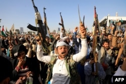 Houthi fighters brandish weapons during a protest following U.S. and British forces strikes, in the Houthi-controlled capital of Sanaa, Jan. 12, 2024.