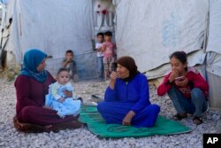 FILE - Syrian family members sit in front of their tent at a refugee camp in Bar Elias, Lebanon, on June 13, 2023. Experts warn that without much more humanitarian assistance, more Syrian refugees could flood into Lebanon and other nearby nations.