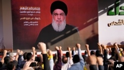 Supporters of the Iranian-backed Hezbollah group raise their fists and cheer as Hezbollah leader Hassan Nasrallah appears via a video link during a rally in Beirut, Lebanon, Nov. 3, 2023. 