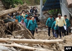 South Korea's President Yoon Suk Yeol (C) walks past piles of fallen trees at a village, where more than a third of houses were damaged in landslides and two people remain missing, in Yecheon on July 17, 2023.