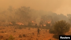 Firefighters try to extinguish a wildfire burning near the village Vlyhada, near Athens, Greece, July 19, 2023.