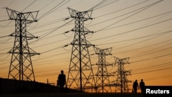 FILE - Locals walk past electricity pylons in Soweto, South Africa, July 3, 2022. Matshela Koko, the former head of the country's power provider Eskom has been charged with multiple counts related to corruption, fraud and money laundering.