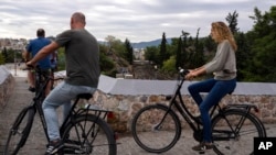 FILE - Tourists cycle on a bridge over subway track near the Thission, Greece, train station, Sept. 21, 2022. 