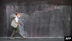 FILE - A woman walks past graffiti on an immigration detention hotel in Melbourne on March 24, 2022.
