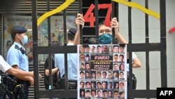 FILE - A protester stands behind mock jail bars with photos of 47 imprisoned pro-democracy figures to be tried under a new national security law, in Hong Kong, Sept. 19, 2021.