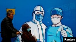 FOTO FILE: Seorang pria mendorong seorang perempuan yang duduk di kursi roda, melewati poster bergambar petugas medis di stan pengujian COVID-19 di Beijing, China, 27 Oktober 2022. (REUTERS/Tingshu Wang/File Foto)