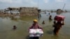 Women carry belongings salvaged from their flooded home after monsoon rains, in the Qambar Shahdadkot district of Sindh Province, of Pakistan, Sept. 6, 2022. 