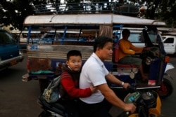 FILE - A Lao boy holds his father as he goes to school on a scooter, in the capital Vientiane, Laos.