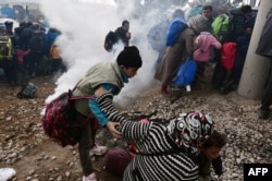 A woman falls as refugees with their children run away after Macedonian police used tear gas to dispearse refugees trying to break the gate to enter Macedonia, Feb. 29, 2016.