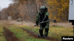FILE - A Ukrainian service member, wearing protective gear, demonstrates using equipment to detect mines in a field, amid Russia's invasion, in the Kharkiv region of Ukraine, Oct. 27, 2022.