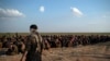 FILE - U.S.-backed Syrian Democratic Forces fighters stand guard next to men waiting to be screened after being evacuated out of the last territory held by Islamic State group militants, near Baghouz, eastern Syria, Feb. 22, 2019.