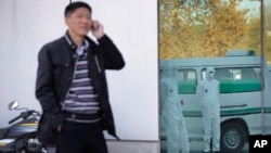 FILE - Photo shows a North Korean man speaking on his mobile phone as medical personnel dressed in protective suits wait by an ambulance, at the Sunan International Airport, in Pyongyang, North Korea, Oct. 27, 2014.