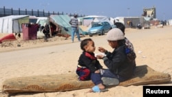 Displaced Palestinian girl, who fled her house due to Israeli strikes, feeds her brother at a tent camp, near the border with Egypt, in Rafah in the southern Gaza Strip, Feb. 25, 2024. 