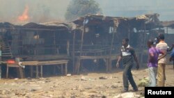 Men stand and watch as a fire rages in the background during clashes between rival gangs in Marche Madina, in Conakry Mar. 1, 2013