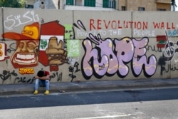 An anti-government protester rests on a sidewalk as others block a main highway in Beirut, Lebanon, Nov. 4, 2019.