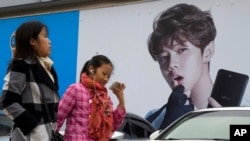 FILE - Women walk past an ad featuring teen idol Lu Han in Beijing, Oct. 21, 2017. China's government banned effeminate men on TV and told broadcasters Sept. 2, 2021, to promote "revolutionary culture." 