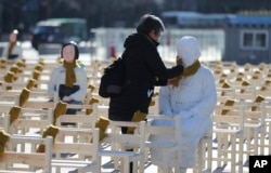 FILE - A woman puts a scarf on a statue of a comfort woman sitting in a installation of empty chairs symbolizing the victims in Seoul, South Korea, Dec. 27, 2017.