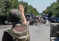 FILE - A member of the Ukrainian State Border Guard Service signals for people to stop as they approach a checkpoint at the contact line between Russia-backed rebels and Ukrainian troops, in Mayorsk, eastern Ukraine, July 3, 2019.