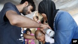 Parents from Syria use water to cool their baby as they wait to cross the border from the northern Greek town of Idomeni to southern Macedonia, Sept. 3, 2015.
