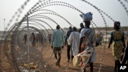 FILE - Displaced people walk next to a razor wire fence at the United Nations base in the capital Juba, South Sudan, Jan. 19, 2016.