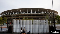 Pedestrians wearing protective masks, following the coronavirus disease (COVID-19) outbreak, walk in front of the National Stadium, the main stadium of Tokyo 2020 Olympics and Paralympics in Tokyo, Japan, July 7, 2021. 