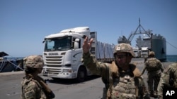 A U.S. Army soldier gestures as trucks loaded with humanitarian aid arrive at the U.S.-built floating pier Trident before reaching the beach on the coast of the Gaza Strip, June 25, 2024.