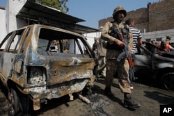 A Pakistani soldier walks past damaged vehicles at the site of a deadly suicide bombing in Charsadda, Pakistan, Monday, March 7, 2016.