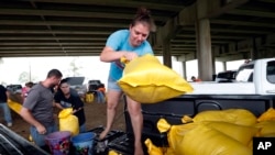 Tiffany Delee tosses a filled sandbag into the back of the family truck, while her husband Mike Delee, left, readies to tie up another bag, in Morgan City, La., July 12, 2019. 