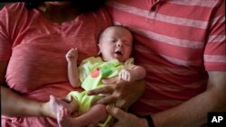 FILE- A couple from Britain hold their baby, born by a surrogate, in Anand, India, Nov. 5, 2015. The Indian government hopes to ban foreigners, single parents and gay couples from using country's surrogacy services in order to protect poor women from exploitation.