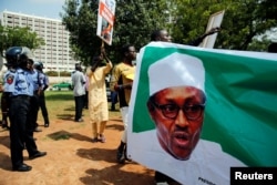 FILE - Supporters of President Muhammadu Buhari rally in support of his administration as police officers look on, at the Unity fountain in Abuja, Nigeria, Aug. 11, 2017.