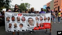 Protesters hold a banner featuring resigned Gov. Ricardo Rosselló, center, amid other politicians that reads "The 12 disciples of evil. Them too." as they demand the resignation of Justice Secretary Wanda Vazquez in San Juan, Puerto Rico, July 29, 2019.