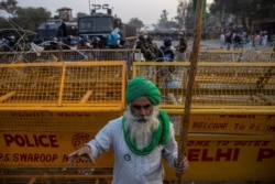 A farmer stands in front of police barricades during a protest against the newly passed farm bills at Singhu border near Delhi, India, Dec. 3, 2020.