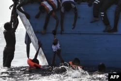 FILE - Migrants try to pull a child out of the water as they wait to be rescued in the Mediterranean Sea, some 12 nautical miles north of Libya, Oct. 4, 2016.