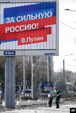 A municipal worker collects rubbish under an election poster for Russian President Vladimir Putin in St. Petersburg, Russia, March 17, 2018. The sign on poster reads: "For the strong Russia! Vladimir Putin."