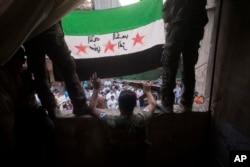FILE - Free Syrian Army rebels hold a revolutionary flag during a demonstration in the Bustan al-Qasr neighborhood of Aleppo, Syria.
