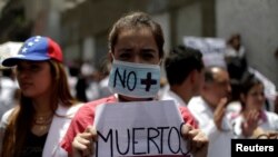 A woman wears a mask and a banner that read "No more deaths" as she takes part in a rally of workers of the health sector against President Nicolas Maduro's government in Caracas, Venezuela, May 17, 2017. 