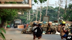 Anti-coup protesters squat behind a barricade that separates them from security forces on the opposite side of the road, in the Dala township of Yangon, Myanmar, Mar. 26, 2021.