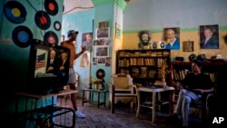 FILE - A man watches President Donald Trump's inauguration speech on television as he sits next to photographs of Cuba's President Raul Castro, top right, former President Fidel Castro, top center, and revolutionary Camilo Cienfuegos, in Havana, Jan. 20, 2017.