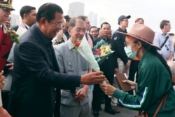 FILE - Cambodian Prime Minister Hun Sen gives flowers to a passenger who disembarked from the MS Westerdam at the port of Sihanoukville, Cambodia, Feb. 14, 2020.