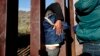 FILE - A Honduran migrant helps a youth squeeze through the U.S. border wall over to San Diego, California, from Playas in Tijuana, Mexico.