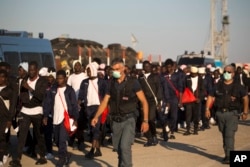 FILE - Italian border police officers escort sub-Saharan men on their way to a relocation center, after arriving aboard the Golfo Azzurro rescue vessel at the port of Augusta, in Sicily, Italy, June 23, 2017.