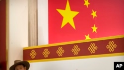 A Tibetan man sits near a mural depicting the Chinese flag at the State Council Information Office in Beijing, Sept. 12, 2019. 