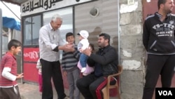 Hussain Ali smiles as he plays with an infant outside his small shop in Domiz, Iraq (VOA).