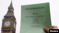 A journalist poses with a copy of the Brexit Article 50 bill, introduced by the government to seek parliamentary approval to start the process of leaving the European Union, in front of the Houses of Parliament in London, Jan. 26, 2017.