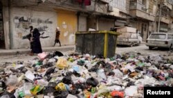 Women walk past piled up garbage after rebels took the main northern city of Aleppo and have since pushed south from their enclave in northwest Syria, Dec. 4, 2024.